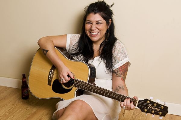 Celeigh Cardinal smiling and playing acoustic Takamine guitar
