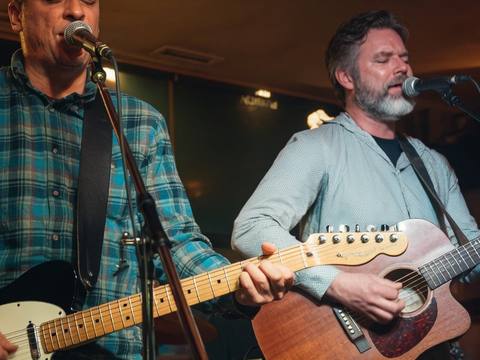 Lead vocalist and guitarist performing together at a club show under warm lighting