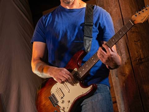 Close-up of guitarist in blue shirt focused on playing at an intimate timber-walled venue, Visualz photo